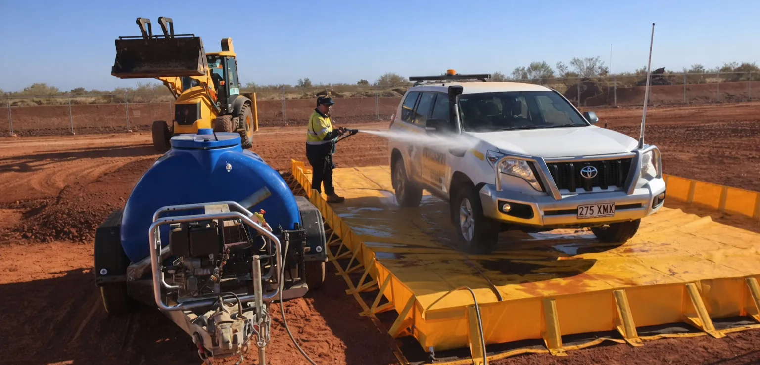 Operator washing a white 4WD in a contained washdown area on a red-earth project site