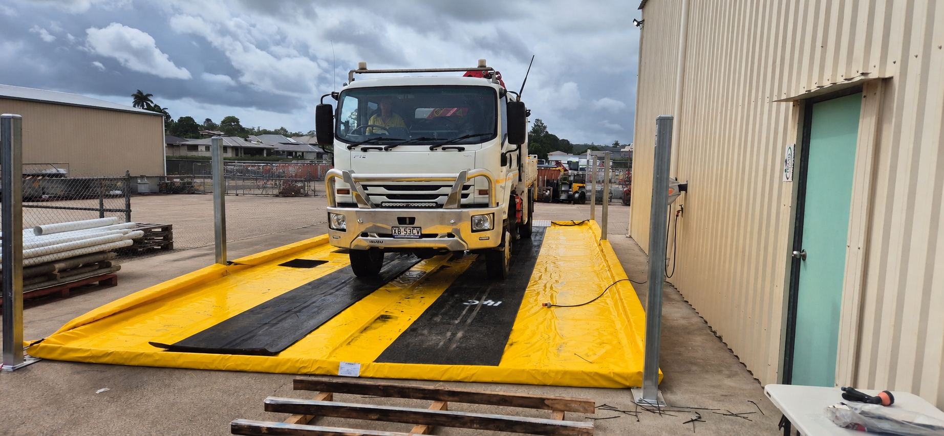 Truck on a yellow vehicle wash mat with black wheel tracks at an outdoor worksite
